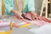 Close up seamstress cutting fabric with scissors in sewing workshop &copy; freepik
